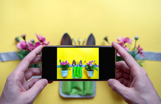 Florist video blog. Hands of a young man with a phone taking pictures of a layout for home gardening on a yellow background.