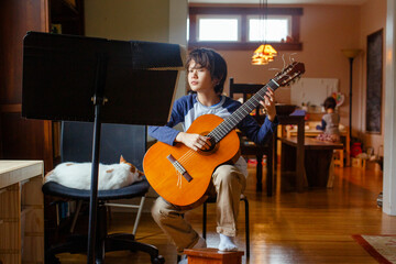 A boy sits quietly next to cat playing guitar while sister sits behind