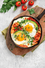 Shakshouka with avocado in a frying pan on a gray table top view. Shakshouka of tomato sauce, eggs, spices, onions, garlic, and avocado. Tasty Maghreb style breakfast. Copy space for text.