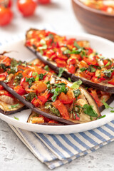 Baked eggplant with tomatoes, peppers, onions, parsley, and olive oil in a plate on a gray concrete table close-up. Tasty vegetarian food Mediterranean style.
