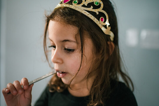 4 year old girl wearing tiara and eating from measuring spoon