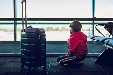 Young boy next to suitcase looking out the window at airport.