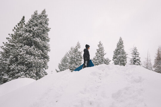 Boy Stands on top of a Snowy Hill with Sled
