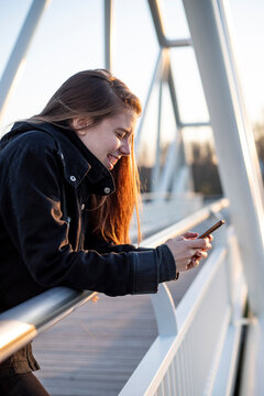 young adult woman laughing in a footbridge with her phone