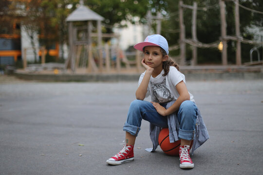 The girl sits on a ball in the playground.