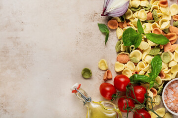 Raw orecchiette with parmesan cheese, tomatoes, basil, garlic and oil on light background with pepper on light brown background. Traditional ingredients for preparation of Italian pasta. Top view.
