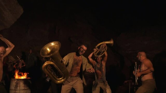 Funny musicians play underground in a cave at night. Crazy people play musical instruments and dance funny dances in the cave. Funny bass guitarist, tubist, trumpeter, drummer. Crazy orchestra playing
