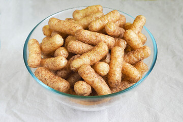 glass bowl with gluten-free corn sticks with cocoa on a beige tablecloth side view . sweet snacks for breakfast for children