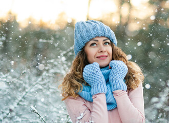 Winter portrait of young beautiful curly brunette woman wearing grey knitted sweater covered in snow. Model looking aside. Snowing winter beauty fashion concept.