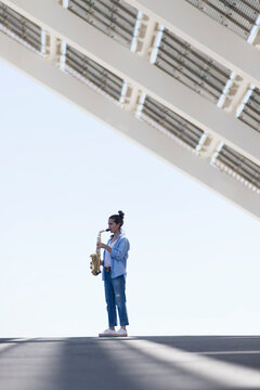 Woman with ponytail playing a saxophone while standing outdoors
