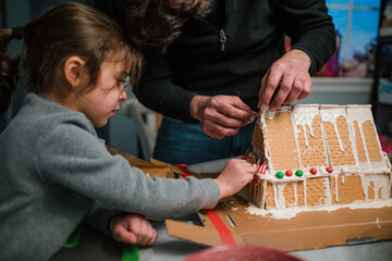 Dad and daughter building gingerbread house in kitchen
