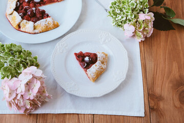 Delicious freshly baked vegan strawberry and cherry galette on wooden rustic background with hydrangea flowers. Sweet food, summer dessert.