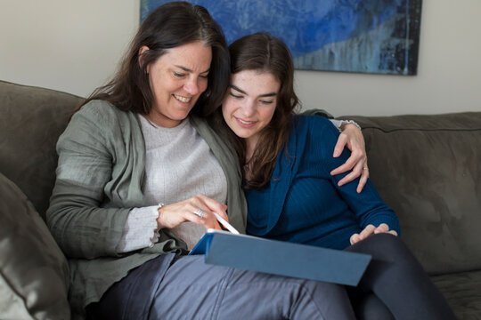 Mother with arm around teen daughter smiling and looking at tablet