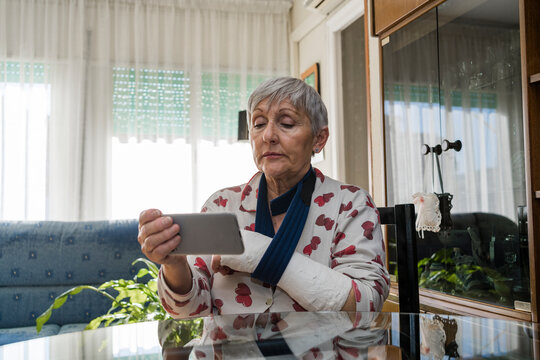Caucasian white-haired elderly woman with broken arm, sitting at home