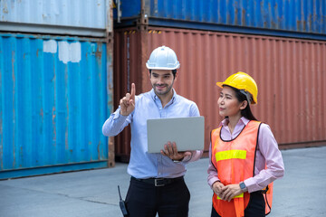 Caucasian shipping officer holding laptop and pointing finger in the air and Asian shipping worker looking at his finger in container shipyard.