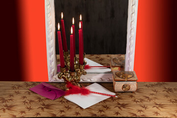 There are burning candles in a candlestick near the mirror. Nearby lies a sheet of paper and a pen with a feather.