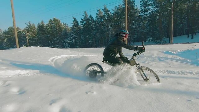 Cyclist in Black Clothes, Helmet and Snow Glasses Riding on Electric Bike in the Snow in Winter Forest. E-Bike Riding and Drifting at Cold Sunny Day - Super Slow Motion