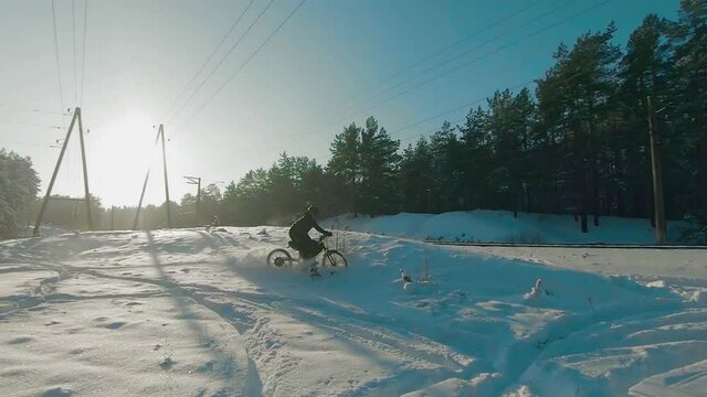 Cyclist in Black Clothes, Helmet and Snow Glasses Riding on Electric Bike in the Snow in Winter Forest. E-Bike Riding and Drifting at Cold Sunny Day - Super Slow Motion
