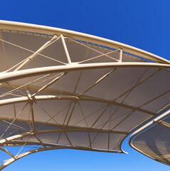 Closeup of a modern tensile structure on a clear blue sky, membrane canvas roof with white steel poles. Photography, full frame.