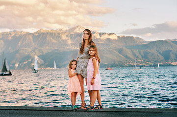 Outdoor portrait of young mother with 2 little daughters, nice summer day by the lake