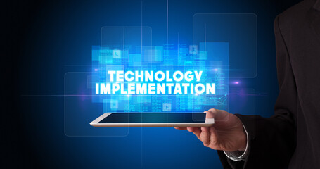 Young business person working on tablet and shows the inscription: TECHNOLOGY IMPLEMENTATION