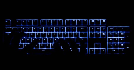 Hands typing in the dark on illuminated keyboard