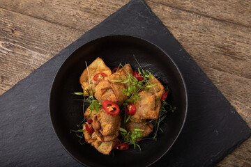 Deep fried, crispy dumplings  in black bowl on black slate