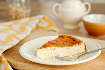 Closeup view of slice of tasty homemade cheesecake on a white porcelain plate with a fork, wooden tray and yellow dishcloth. Selective focus.