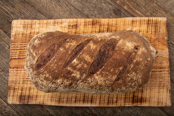 Freshly baked loaf of bread on wooden board, isolated on wooden table