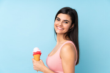 Young woman holding a cornet ice cream over isolated blue background smiling a lot