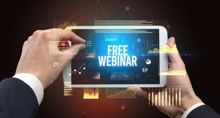 Close-up of hands holding tablet with FREE WEBINAR inscription, modern business concept