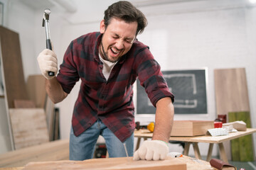 Hammering fail. A carpenter wearing a red flannel shirt, jeans and cloth protective gloves...
