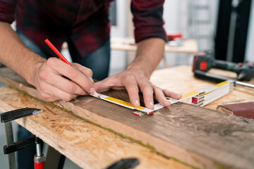 Close-up of a hardworking professional carpenter holding a angular ruler and pencil while measuring...