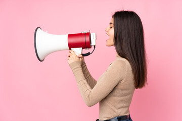 Young woman over isolated pink background shouting through a megaphone