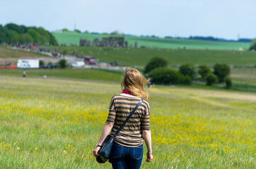 Woman walking on the Salisbury plain with the blurred Stonehenge in the distance, Wiltshire,...