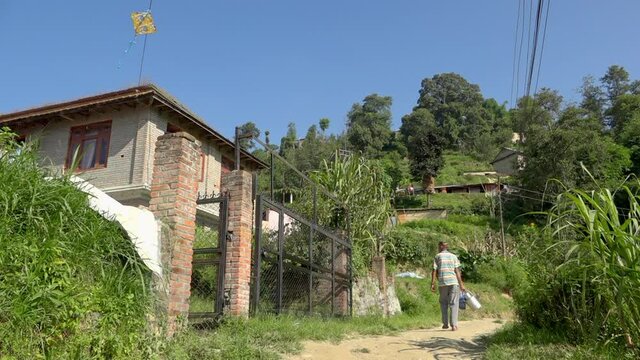 Man carrying milk canisters past rural house, Banepa, Bagmati Province, Nepal