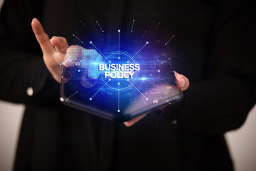 Naklejka premium Businessman holding a foldable smartphone with BUSINESS POLICY inscription, new business concept