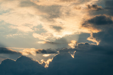 Sunbeams filter through cumulus nimbus under high altitude clouds.