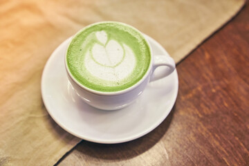 Cup of matcha latte on wooden background and napkin in a cafe with copy space