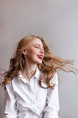 Inspired blonde woman posing with closed eyes. Studio shot of relaxed girl in white shirt.