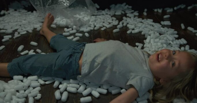 A little preschooler is lying on the floor making snow angels with styrofoam balls