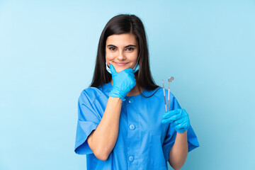 Young woman dentist holding tools over isolated blue background laughing