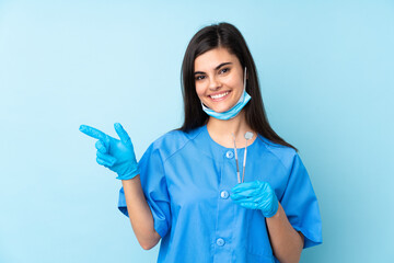 Young woman dentist holding tools over isolated blue background pointing finger to the side