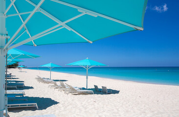 Fototapeta na wymiar Grand Cayman Beach Deck Chairs Blue Umbrellas On Water's Edge.Caribbean, Grand Cayman, Seven Mile Beach, Cayman Islands, Palm Trees. Empty beach, No tourists