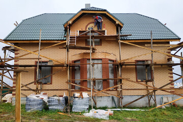 Fototapeta na wymiar The house made of foam concrete, insulated with mineral wool and lined with facade brick, has a scaffolding near the house.