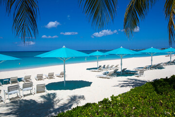 Grand Cayman Beach ligstoelen blauwe parasols aan de rand van het water. Caribbean, Grand Cayman, Seven Mile Beach, Kaaimaneilanden, palmbomen. Leeg strand, geen toeristen