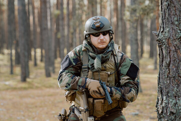Fototapeta premium Portrait of a middle-aged bearded soldier in a Woodland military uniform and helmet, with headphones on his head holding a gun.