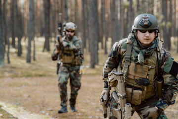 Portrait of a middle-aged bearded soldiers in a Woodland military uniform and helmet, with headphones on his head holding a gun.