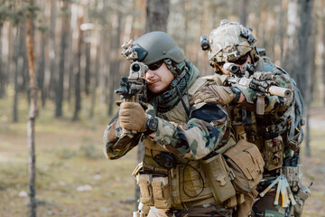 A soldier in a special military uniform, with a helmet on his head and with a sniper rifle in the...