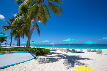 Grand Cayman strandstoelen blauwe parasols aan de rand van het water. Caraïben, Grand Cayman, Seven Mile Beach, Kaaimaneilanden, palmbomen. Leeg strand, geen toeristen